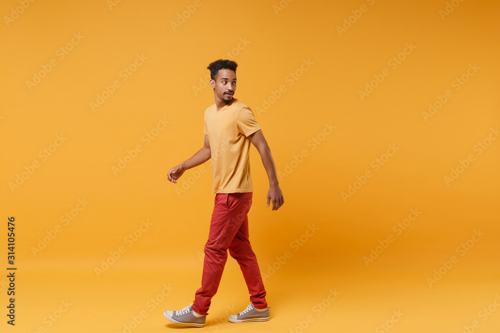 Side view of young african american guy in casual clothes posing isolated on yellow orange wall background studio portrait. People sincere emotions lifestyle concept. Mock up copy space. Looking back. Side view of young african american guy in casual clothes posing isolated on yellow orange wall background studio portrait. People sincere emotions lifestyle concept. Mock up copy space. Looking back.