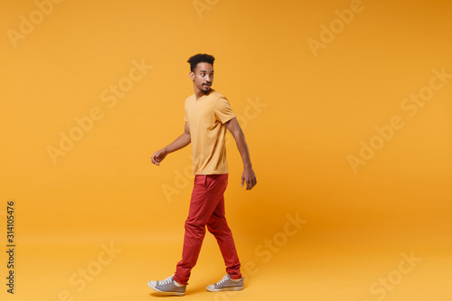 Side view of young african american guy in casual clothes posing isolated on yellow orange wall background studio portrait. People sincere emotions lifestyle concept. Mock up copy space. Looking back.