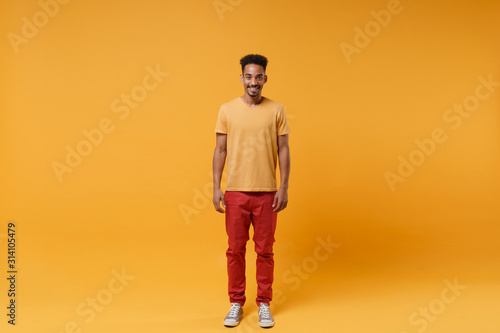 Smiling young african american guy in casual clothes posing isolated on yellow orange wall background, studio portrait. People sincere emotions lifestyle concept. Mock up copy space. Looking camera.