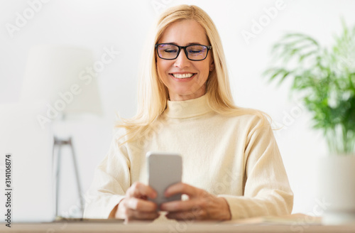 Middle-aged woman websurfing on cellphone, wearing glasses