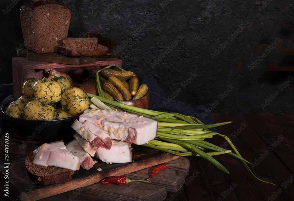 Lard, boiled potatoes, bread, cucumbers and green onions on a wooden background. Russian and Ukrainian traditional appetizer, black bread and lard. A delicious snack with bacon