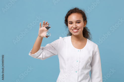 Smiling african american doctor woman isolated on blue wall background. Female doctor in white medical gown hold hourglass black sand. Healthcare personnel medicine health concept. Mock up copy space.