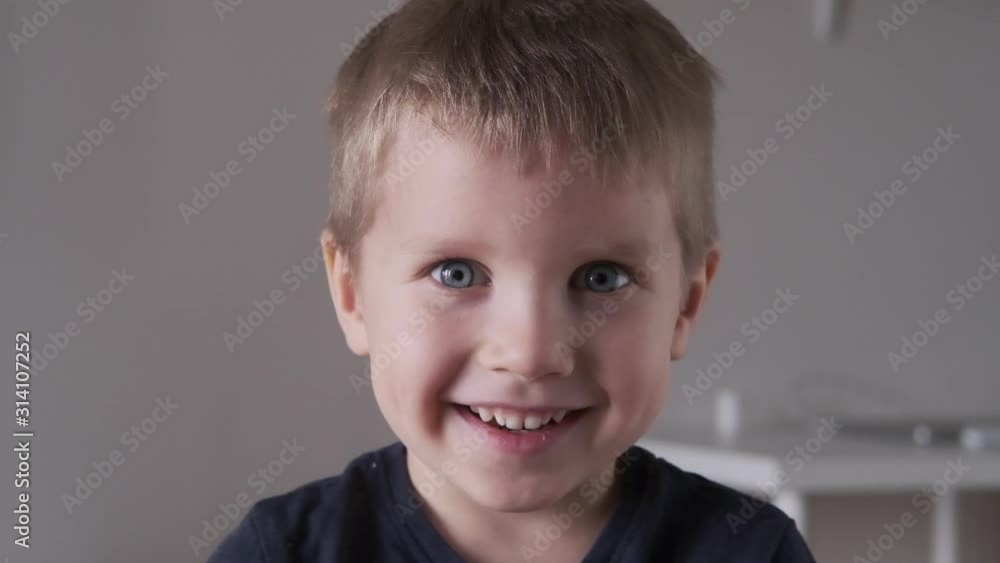 Adorable happy kid baby boy is looking to the camera. Baby looks around and then smiles and laughs. 4 years old fair-haired child with blue eyes smiles at home Adorable happy kid baby boy is looking to the camera. Baby looks around and then smiles and laughs. 4 years old fair-haired child with blue eyes smiles at home