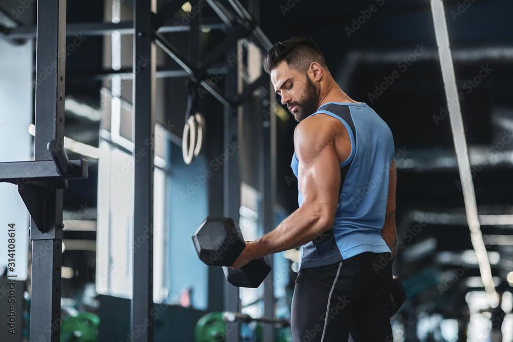 Handsome athlete training arms with dumbbells at gym