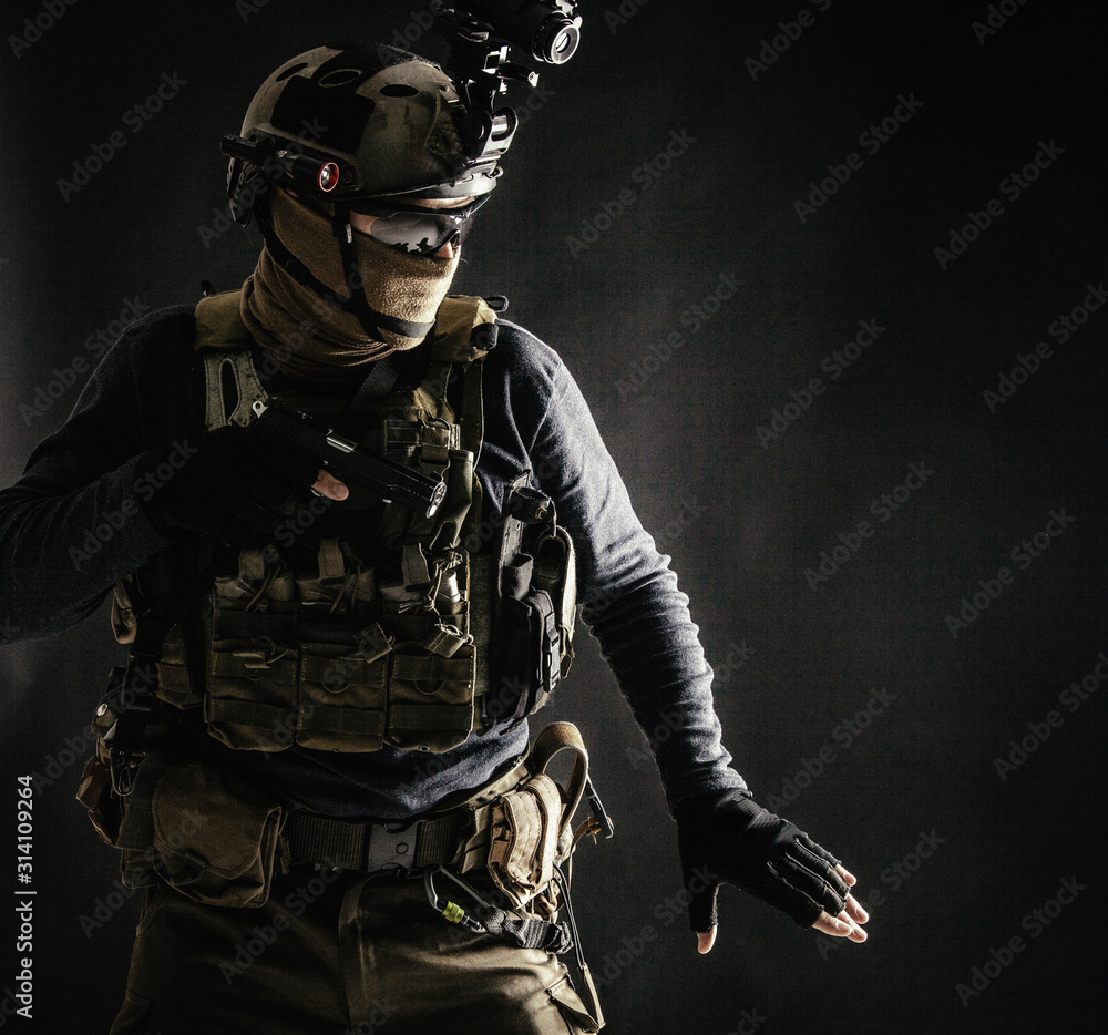 Special operations fighter in helmet with night-vision, thermal imaging device, load carrier carefully moving with caution in darkness, holding hand on pistol, ready for fight during dangerous mission