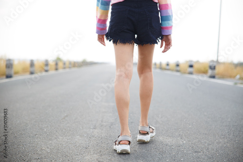 Young woman walking on the road with white sky background.