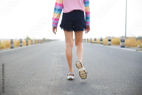 Young woman walking on the road with white sky background.