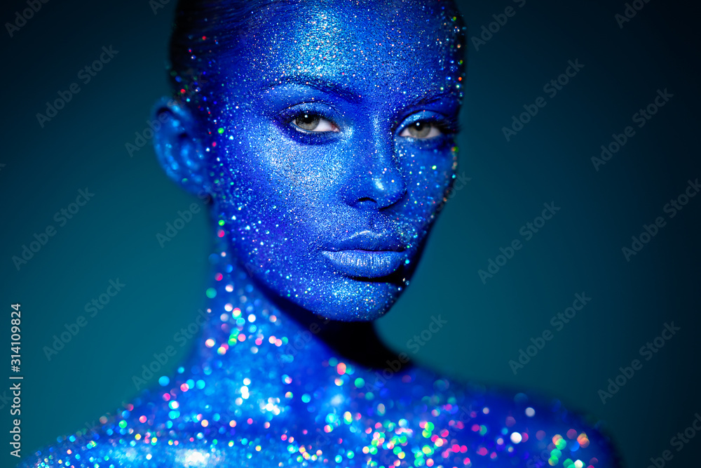 Fototapeta Fashion model woman in blue bright sparkles and neon lights posing in studio. Portrait of beautiful sexy woman. Art design colorful glitter glowing make up