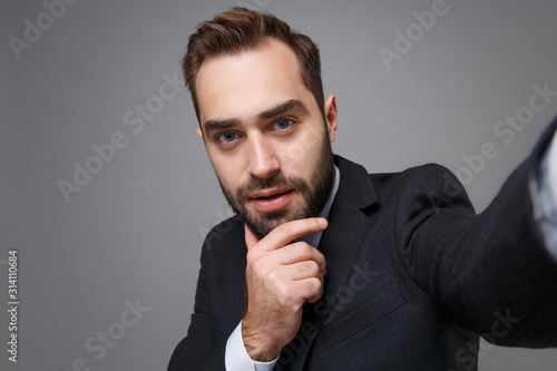 Close up of business man in suit shirt posing isolated on grey background. Achievement career wealth business concept. Mock up copy space. Doing selfie shot on mobile phone put hand prop up on chin.