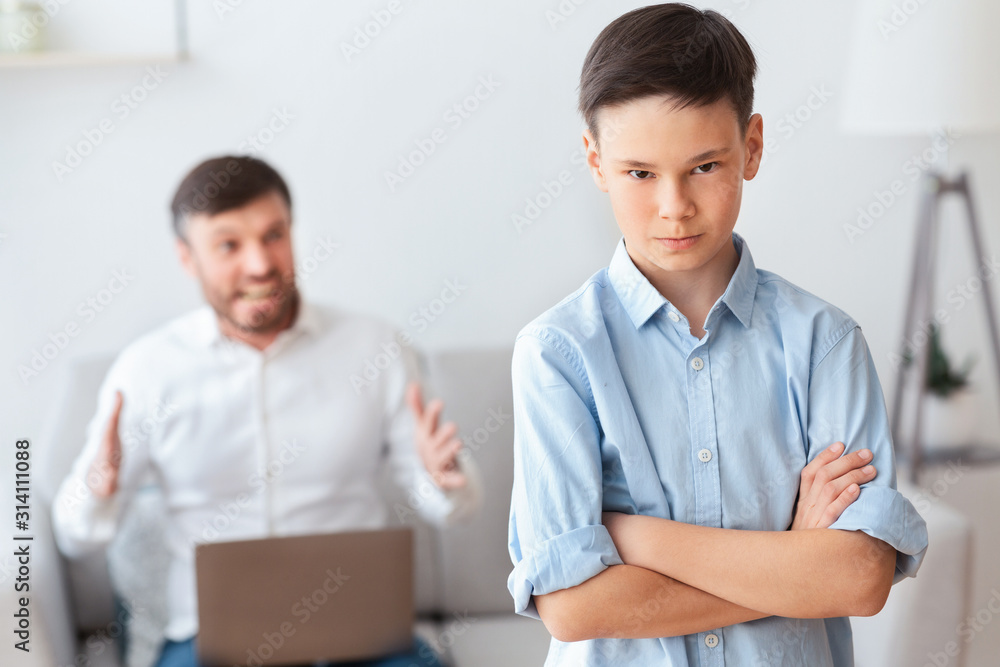 Furious Father Shouting At Son Sitting On Sofa At Home Furious Father Shouting At Son Sitting On Sofa At Home