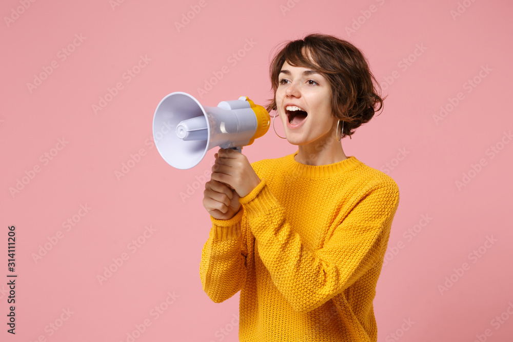 Cheerful young brunette woman girl in yellow sweater posing isolated on pastel pink background studio portrait. People sincere emotions lifestyle concept. Mock up copy space. Screaming in megaphone. Cheerful young brunette woman girl in yellow sweater posing isolated on pastel pink background studio portrait. People sincere emotions lifestyle concept. Mock up copy space. Screaming in megaphone.