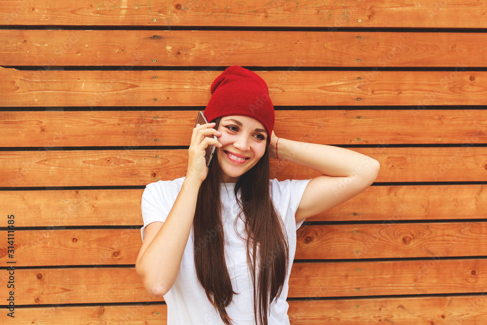 young beautiful girl with a phone smiles near a wooden wall in fashionable youth clothes. young beautiful girl with a phone smiles near a wooden wall in fashionable youth clothes.