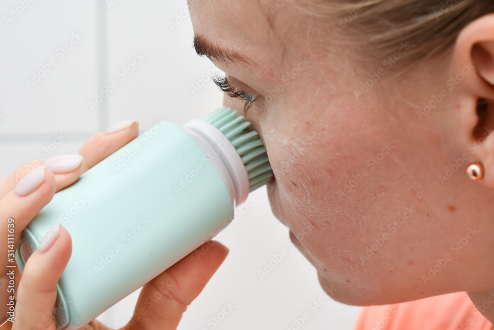 Girl is cleaning face with electric brush. Woman with special brush for deep cleansing facial remove makeup. Skin Care concept. High technology beauty. Girl is cleaning face with electric brush. Woman with special brush for deep cleansing facial remove makeup. Skin Care concept. High technology beauty.