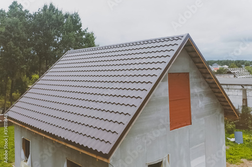 Brown metal tile on the roof of the house. Corrugated metal roof and metal roofing. Modern roof made of met