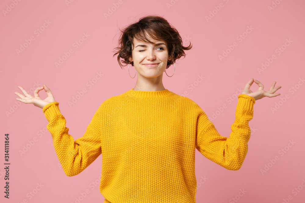 Funny young brunette woman girl in yellow sweater posing isolated on pastel pink background. People lifestyle concept. Mock up copy space. Hold hands in yoga gesture relaxing meditating looking aside. - obrazy, fototapety, plakaty 