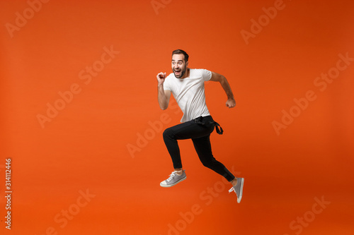 Cheerful funny young man in casual white t-shirt posing isolated on bright orange wall background studio portrait. People lifestyle concept. Mock up copy space. Having fun, fooling around, jumping.