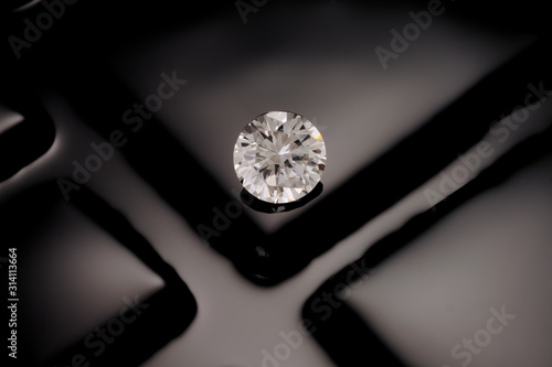 A solitaire, clean, clear, faceted, round diamond sits on a reflective background of black of fuse glass squares.