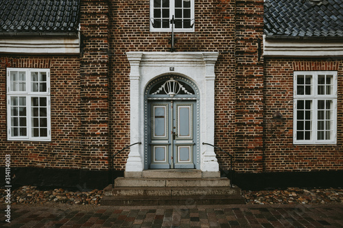 Historic brick house facade with white-framed windows and ornate blue double door, located in Ribe, Denmark, on a rainy autumn day