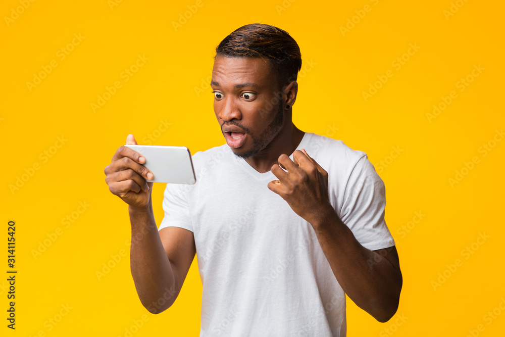 Shocked Afro Guy Looking At Smartphone Standing In Studio - obrazy, fototapety, plakaty 