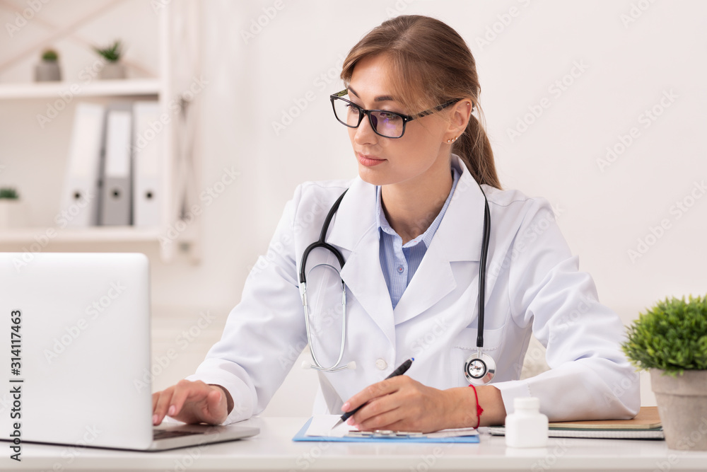 Doctor Woman Working On Laptop Taking Notes Sitting In Office Doctor Woman Working On Laptop Taking Notes Sitting In Office