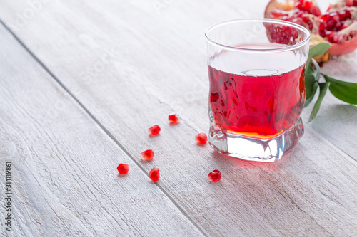 Glass of pomegranate juice and ripe pomegranate on a white wooden background. Healthy drink concept. Сopy space
