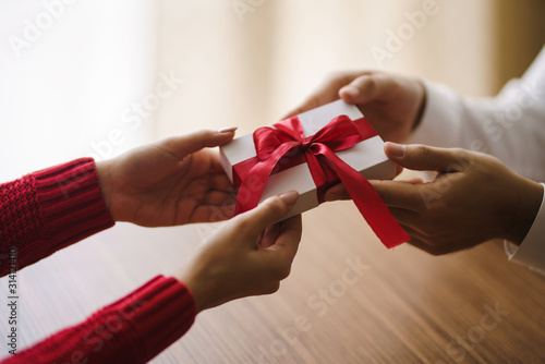 Man gives to his woman a gift box with red ribbon. Hands of man gives surprise gift box for girl. Young loving couple celebrating Valentine's Day. Relationship, surprise, Birthday concept.