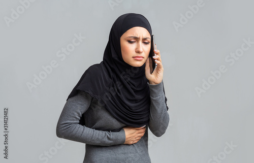 Sick muslim woman suffering from stomach pain, calling doctor for help