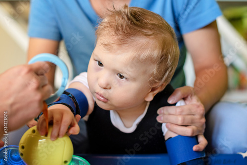 Portrait of a child with cerebral palsy on physiotherapy in a children therapy center. Boy with disability has therapy by doing exercises with physiotherapists in rehabitation centre.