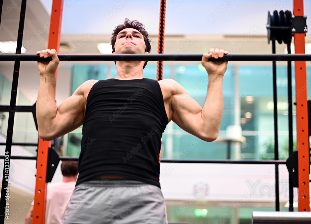 Naklejka premium Man doing free body calisthenic pull-ups in a gym