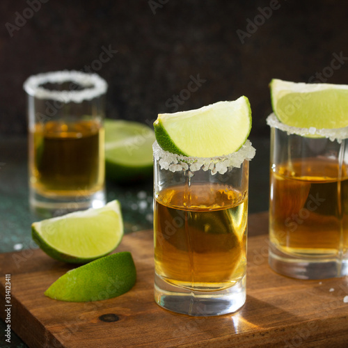Gold Tequila. Mexican Gold Tequila shot with lime and salt on dark stone background.