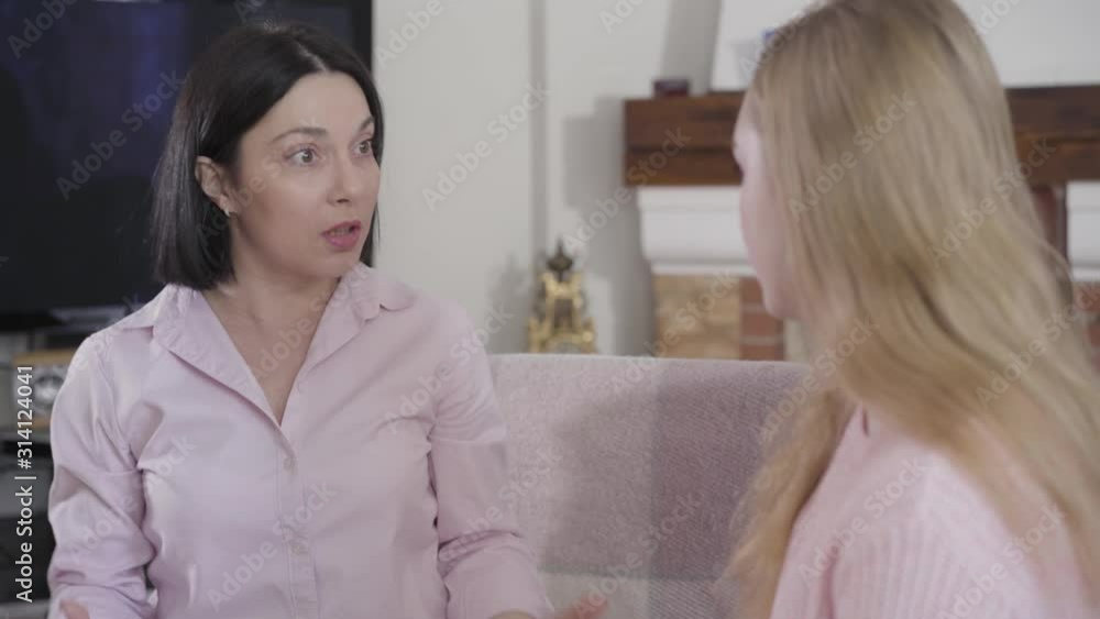 Close-up of young brunette Caucasian woman talking emotionally to blond girl. Mother spending free time with daughter at home. Trust, reliance, family relationship. Close-up of young brunette Caucasian woman talking emotionally to blond girl. Mother spending free time with daughter at home. Trust, reliance, family relationship.