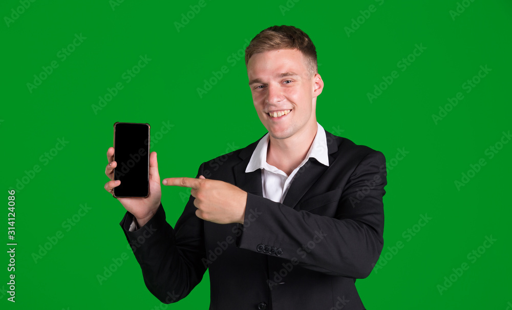 Business man in a jacket points a finger at a smartphone with a blank screen, isolated on a green background. Concept for advertising mobile applications. Business man in a jacket points a finger at a smartphone with a blank screen, isolated on a green background. Concept for advertising mobile applications.