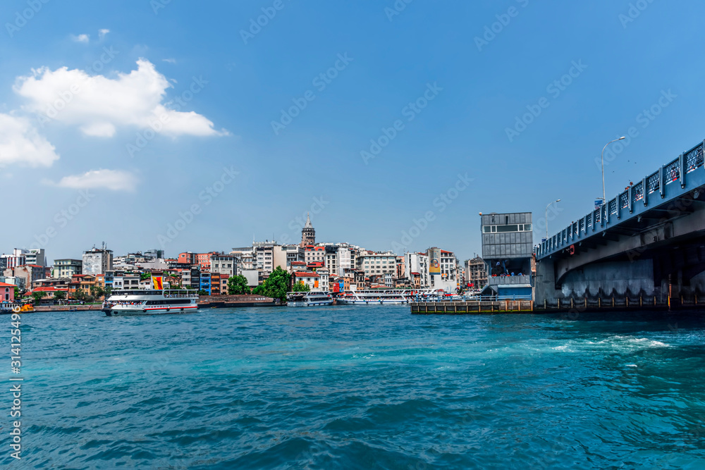 view of the water of the Bosphorus in Istanbul Turkey, with a piece of Galata Bridge on the right, background the buildings on the other side against a blue sky.