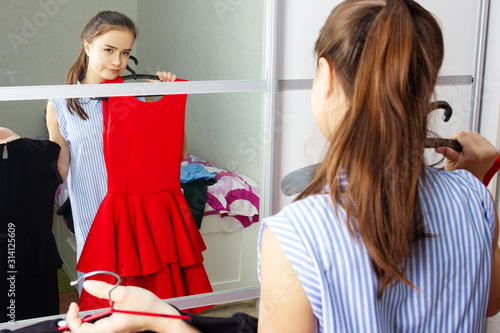 The girl at home in front of the mirror tries on dresses, chooses an outfit photo