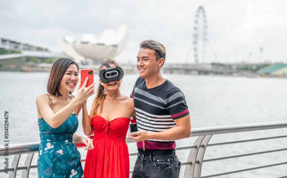 Three asian young friends outdoor wearing vr glasses and taking selfies. Happiness and holiday concept