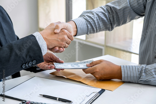 Bribery and corruption concept, bribe in the form of dollar bills, Businessman shaking hands and giving hides money while making deal to agreement a contract