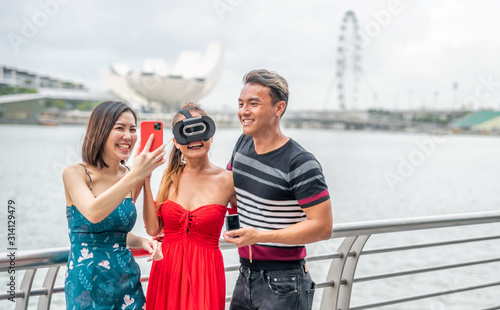 Three asian young friends outdoor wearing vr glasses and taking selfies. Happiness and holiday concept © jovannig