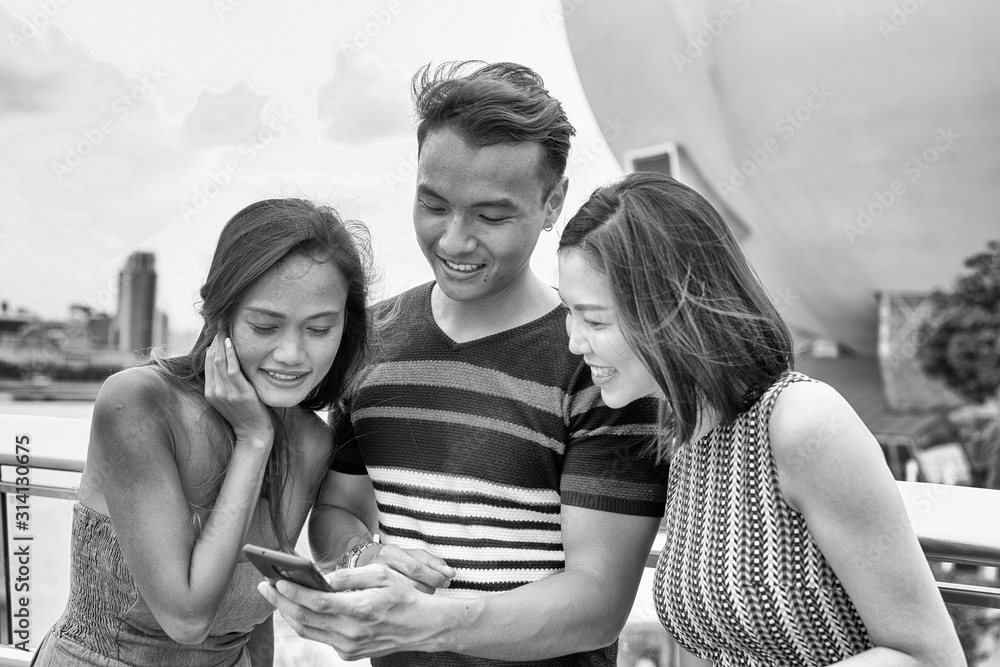 Three young asian friends reviewing city pictures on the smartphone. Tourism and holiday concept