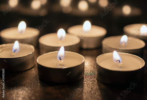 close up of burning candles on black table in the dark with reflection from the background.