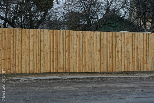 part of a private long brown fence from wooden boards on a rural street by a gray asphalt road