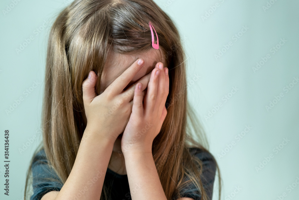 Close-up portrait of unhappy little girl with long hair covering her face with hands crying. Close-up portrait of unhappy little girl with long hair covering her face with hands crying.