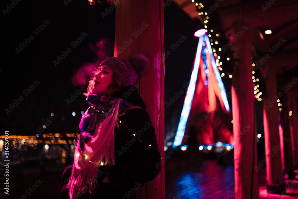 Vapor from mouth - Young attractive redhead girl hanging out in amusement theme park with bright vivid colorful attractions and installations background - Eastern European in Latvia Riga