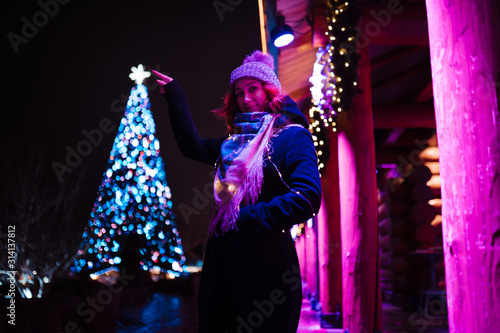 Touching the christmas tree star - Young attractive redhead girl hanging out in amusement theme park with bright vivid colorful attractions and installations background