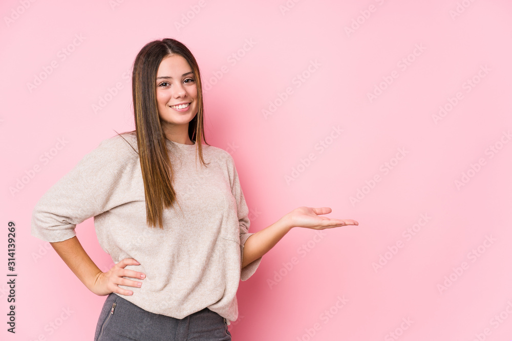 Young caucasian woman posing isolated showing a copy space on a palm and holding another hand on waist. Young caucasian woman posing isolated showing a copy space on a palm and holding another hand on waist.