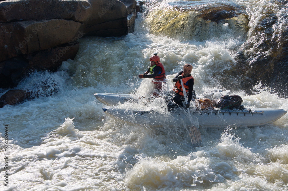 Two athletes on an inflatable catamaran are rafting in a waterfall. Kharlovka River, Kola Peninsula, Russia.