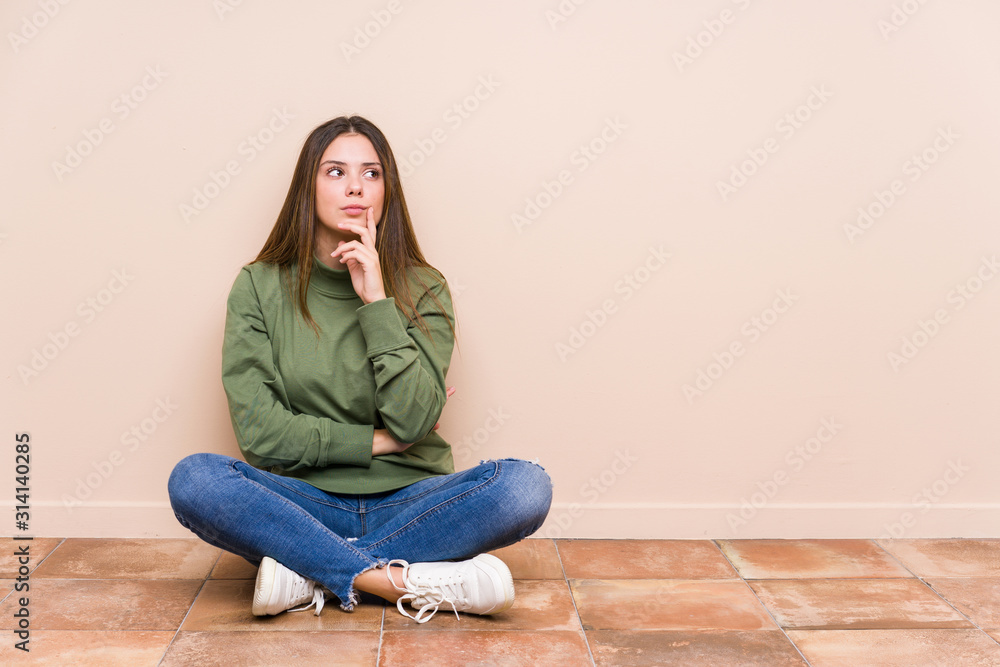 Young caucasian woman sitting on the floor isolated looking sideways with doubtful and skeptical expression. Young caucasian woman sitting on the floor isolated looking sideways with doubtful and skeptical expression.