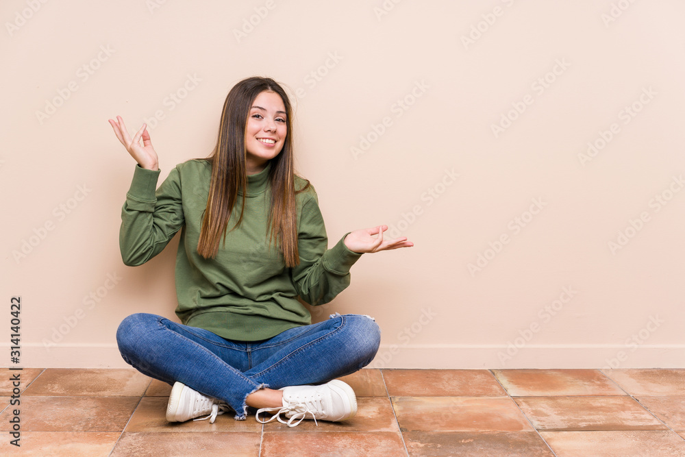 Young caucasian woman sitting on the floor isolated doubting and shrugging shoulders in questioning gesture. Young caucasian woman sitting on the floor isolated doubting and shrugging shoulders in questioning gesture.
