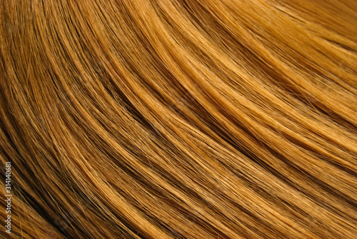 A closeup view of a section of glossy straight ginger hair in a wavy style. Shiny highlight abstract background texture, synthetic extensions. Beauty salon. Hair care, healthy.