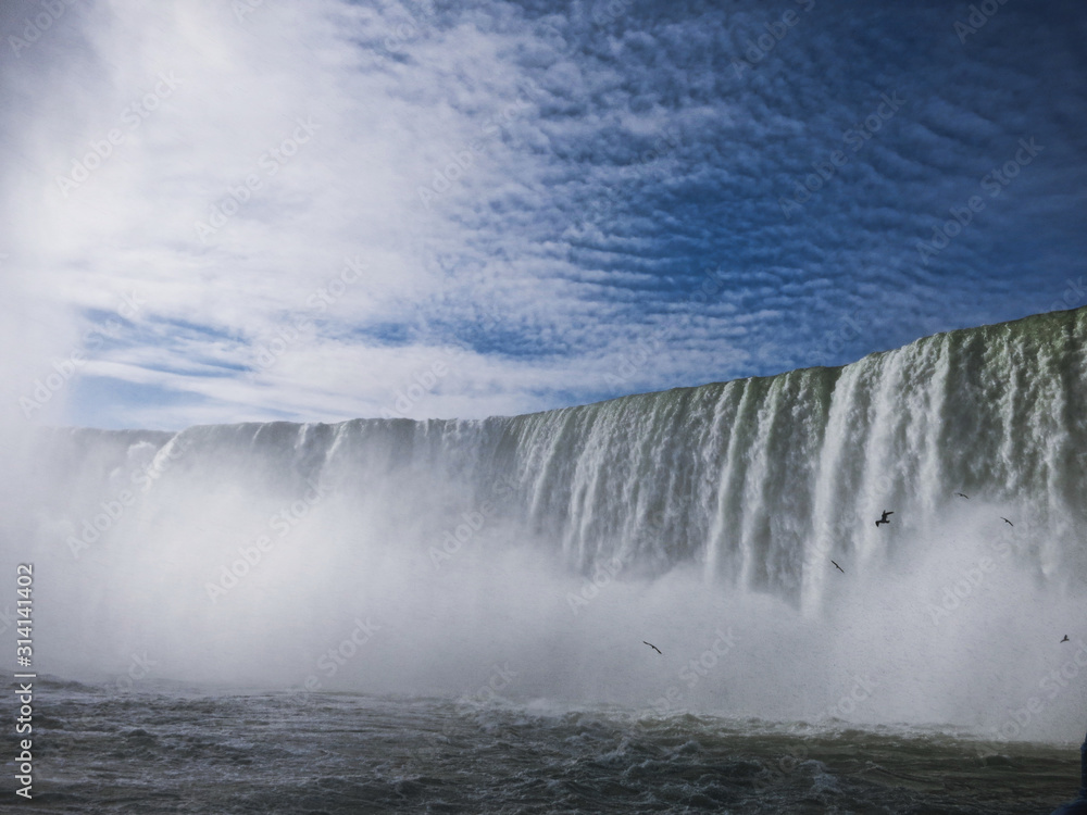 Wasserflut der Niagara Falls vor blauem Himmer und Nebel mit Möwen Wasserflut der Niagara Falls vor blauem Himmer und Nebel mit Möwen
