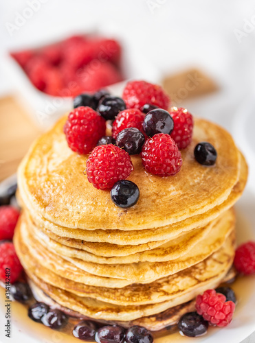 Sweet homemade pancakes with raspberries and blueberries on white plate.